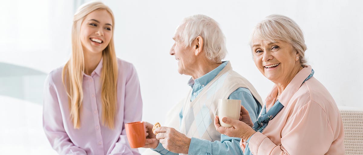 Kaksi ikäihmistä juovat kahvia ja keskustelevat vanhuspalveluohjaajan kanssa.